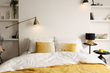 Yatak odasında çarşafları, komodinleri, lambaları ve raf üniteleri olan büyük bir yatak.