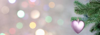 Gri arka plandaki bulanık ışıklara karşı kalp şeklinde süslemeleri olan Noel ağacı dalı, bokeh etkisi. Metin için alanı olan pankart tasarımı