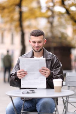 Genç adam açık kafedeki masada gazete okuyor.