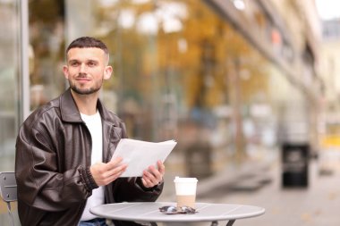 Açık kafedeki masada gazete okuyan genç bir adam. Metin için boşluk