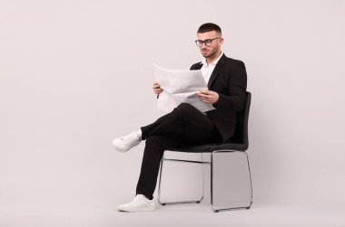 Genç adam açık gri arka planda sandalyede gazete okuyor. Metin için boşluk