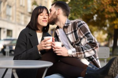 Açık kafede yemek fincanları olan sevimli bir çift. Erkek, kız arkadaşını öpüyor.