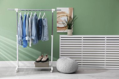 İçerideki yeşil duvarın yanında askıda asılı farklı şık elbiseler, puf ve bitkiler.