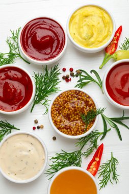 Tabaklardaki farklı soslar ve beyaz ahşap masa üzerindeki malzemeler.