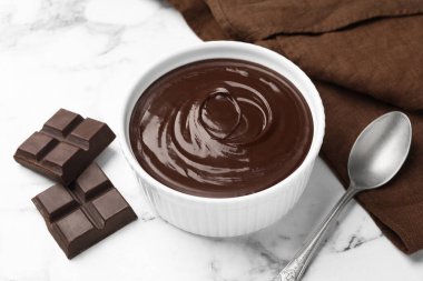 Erimiş çikolata kasede, parçalar ve kaşık beyaz mermer masada, yakın plan.