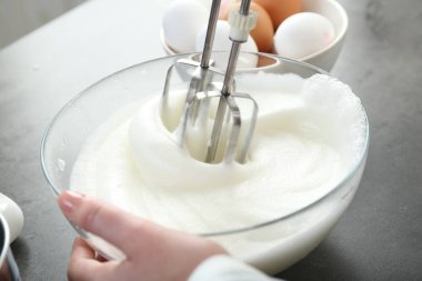 Gri masada yumurta beyazını mikserle döven kadın, yakın plan.