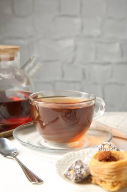 Cam fincanda lezzetli çay, çaydanlık ve Türk tatlıları beyaz masada, arka planda gri dokuya karşı, yakın plan. Metin için boşluk