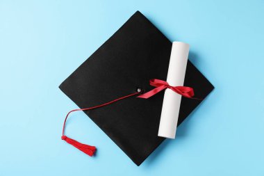 Açık mavi arka planda diploma ve mezuniyet şapkası, üst görünüm