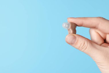 Açık mavi arka planda işitme cihazı olan kadın, yakın plan. Metin için boşluk