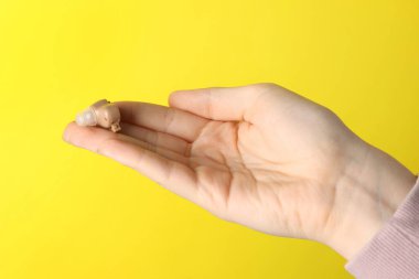 Sarı arka planda işitme cihazı olan kadın, yakın plan.