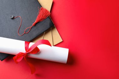Diploma, not defterleri ve kırmızı arka planda mezuniyet şapkası. Metin için boşluk