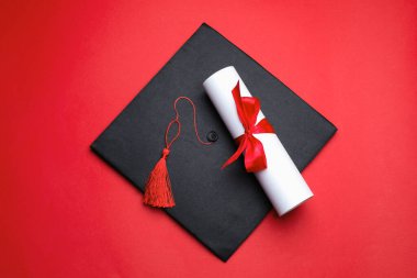 Kırmızı arka planda diploma ve mezuniyet şapkası, üst görünüm
