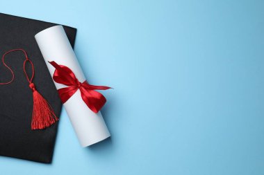 Açık mavi arka planda diploma ve mezuniyet şapkası, üst manzara. Metin için boşluk