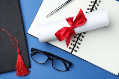 Diploma, mezuniyet şapkası, defter, mavi arka planda gözlük ve kalem.