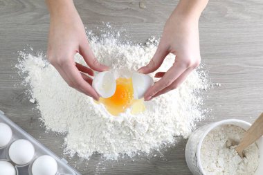 Ahşap masada yumurta kıran bir kadın.