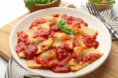 Beyaz ahşap masada servis edilen domates soslu ve fesleğenli lezzetli ravioli.