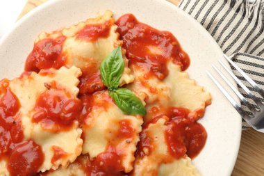 Beyaz ahşap masada servis edilen domates soslu ve fesleğenli lezzetli ravioli.