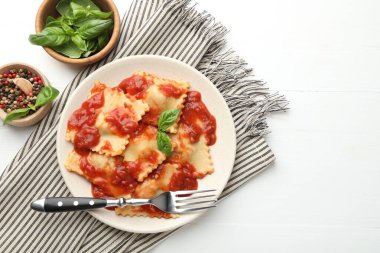 Beyaz ahşap masada servis edilen domates soslu ve fesleğenli lezzetli ravioli. Metin için boşluk