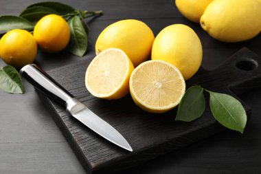 Yeşil yapraklı taze limonlar ve siyah ahşap masada bıçak, yakın plan.