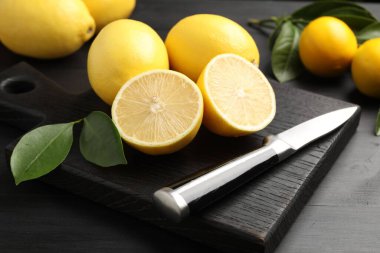 Yeşil yapraklı taze limonlar ve siyah ahşap masada bıçak, yakın plan.