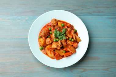 Açık mavi ahşap masada nefis pişmiş yahni.