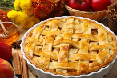 Lezzetli ev yapımı turta, taze elmalar, bal ve çiçekler ahşap masada, yakın plan.