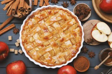 Lezzetli ev yapımı elmalı turta fırın tabağında ve mavi ahşap masada malzemeler var.