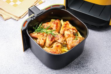 Izgara tavuk kanadı, patates kızartması ve biberiye, hava fritözünde, gri masada, yakın plan.