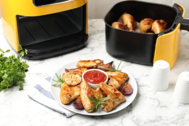 Lezzetli ızgara tavuk kanatları, sos ve baharatlar. Beyaz mermer masada pişirilmiş bagetlerle birlikte.