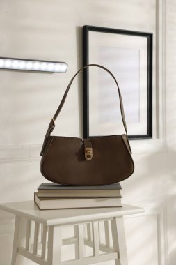 Beyaz duvarda şık bir LED lamba, kitaplarla dolu tabure ve kapalı bir çanta.