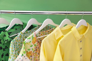 Farklı kadın kıyafetleri yeşil arka planda asılı, yakın plan.