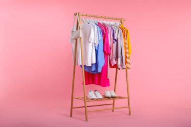 Pembe arka planda asılı farklı kıyafetler, çanta ve ayakkabılar