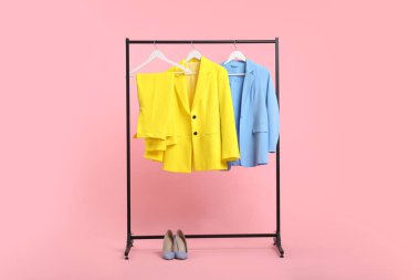 Farklı elbiseler askıda asılı ve pembe arka planda ayakkabılar