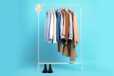 Farklı kıyafetler askıda asılı ve ayakkabılar açık mavi arka planda