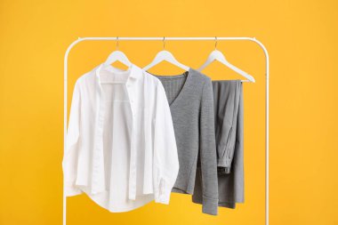 Farklı giysiler turuncu arka planda asılı duruyor.