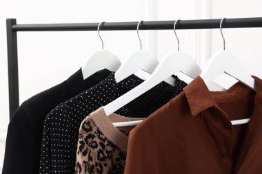 Beyaz duvarın yanında asılı duran farklı kadın kıyafetleri, yakın plan.