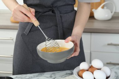 Mutfaktaki beyaz mermer masada çırpılmış yumurta çırpan kadın, yakın plan.