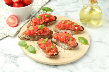Domatesli lezzetli bruschettalar ve beyaz mermer masada fesleğen, yakın plan.