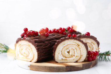 Lezzetli Noel kütüğü (geleneksel Noel pastası) beyaz masa üzerinde kırmızı frenk üzümü, yakın plan