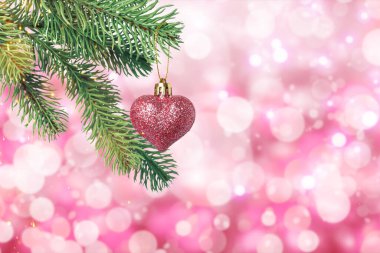 Pembe arka plandaki bulanık ışıklara karşı kalp şeklinde süslemeli Noel ağacı dalı, bokeh etkisi