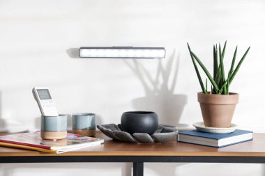 Ahşap masanın üstündeki beyaz duvarda süslü LED lamba. İçinde dergiler ve dekorasyon var.