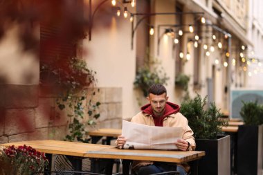 Açık kafedeki masada gazete okuyan genç bir adam. Metin için boşluk