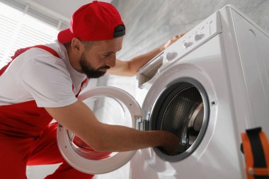 Profesyonel tamirci, bozuk çamaşır makinesini içeride tamir ediyor. Düşük açılı görüntü.