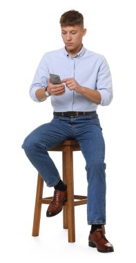 Beyaz arka planda akıllı telefon kullanan şık kotlu yakışıklı bir genç.