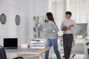 Kadın ve meslektaşı ofiste dart oynuyorlar.