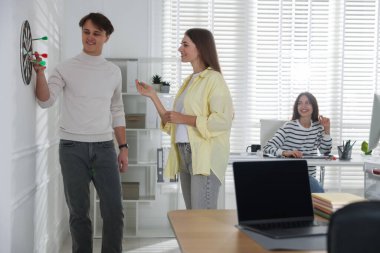 Kadın ve meslektaşları ofiste dart oynuyorlar.