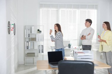 Kadın ve meslektaşları ofiste dart oynuyorlar.