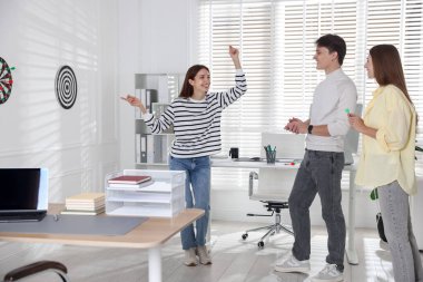 Kadın ve meslektaşları ofiste dart oynuyorlar.