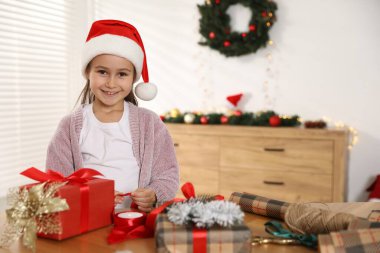 Noel Baba şapkalı küçük kız Noel hediyelerini kapalı bir masada paketliyor. Metin için boşluk