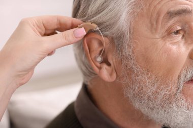 Bakıcı, kıdemli adamın evde işitme cihazı takmasına yardım ediyor.